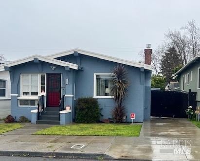 bungalow with stucco siding, a front lawn, concrete driveway, and a chimney