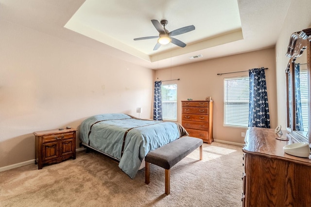 bedroom with visible vents, light colored carpet, a raised ceiling, and multiple windows