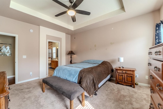 bedroom featuring light colored carpet, baseboards, connected bathroom, and a tray ceiling