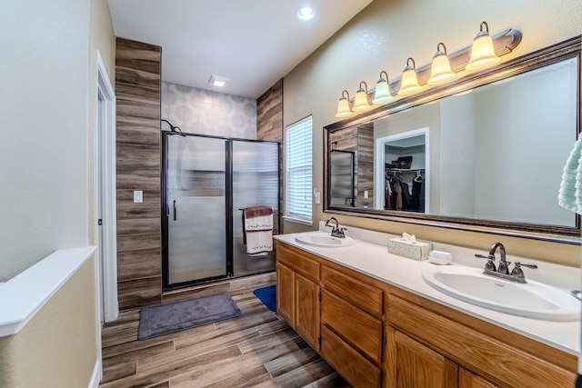 bathroom featuring double vanity, a stall shower, wood finished floors, and a sink