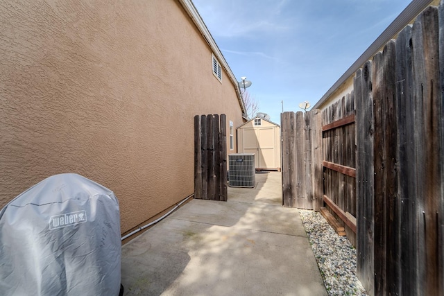 view of side of home with an outbuilding, cooling unit, fence, stucco siding, and a patio area