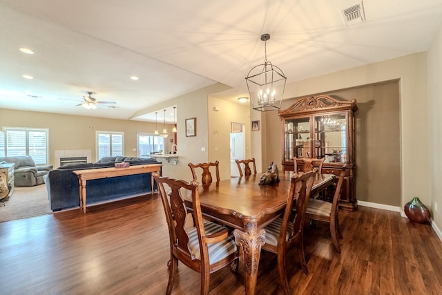 dining space with visible vents, baseboards, dark wood finished floors, a fireplace, and ceiling fan with notable chandelier