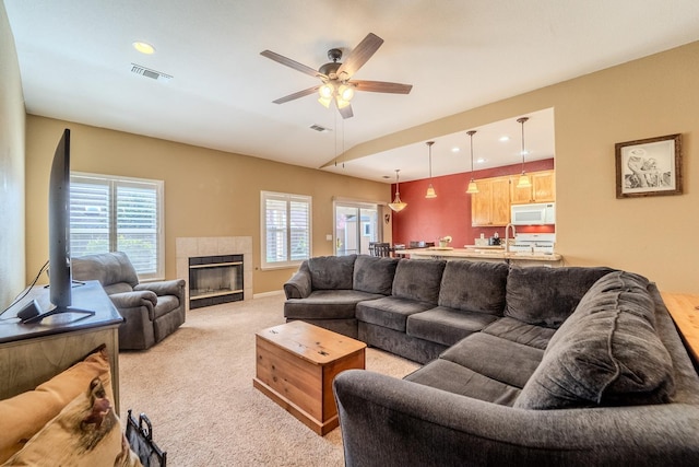 living area featuring light carpet, visible vents, a fireplace, and a ceiling fan