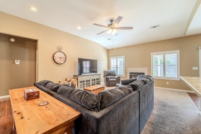 carpeted living area featuring a tiled fireplace, lofted ceiling, baseboards, and visible vents