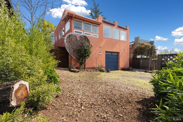 rear view of property featuring dirt driveway, stucco siding, a garage, and fence