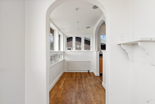 hall featuring lofted ceiling, radiator heating unit, wood finished floors, and baseboards