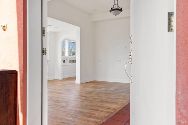 interior space with baseboards, arched walkways, and light wood finished floors