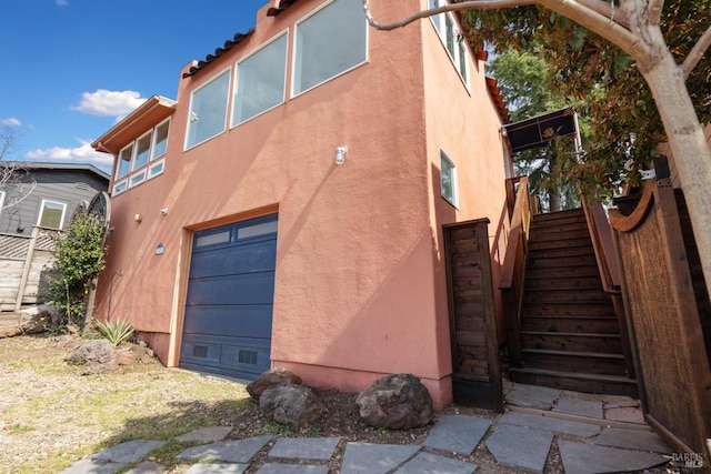 view of side of home with stucco siding, stairway, and a garage