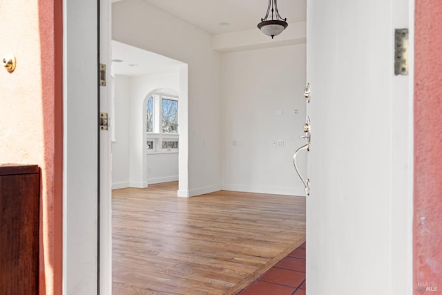 corridor featuring light wood finished floors, baseboards, and arched walkways