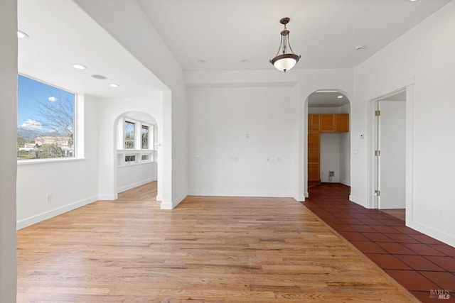 unfurnished dining area with recessed lighting, light wood-style floors, arched walkways, and baseboards