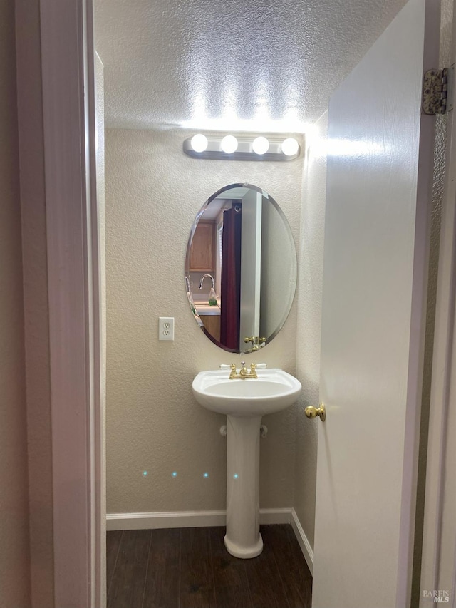 bathroom with wood finished floors, baseboards, a textured wall, and a textured ceiling