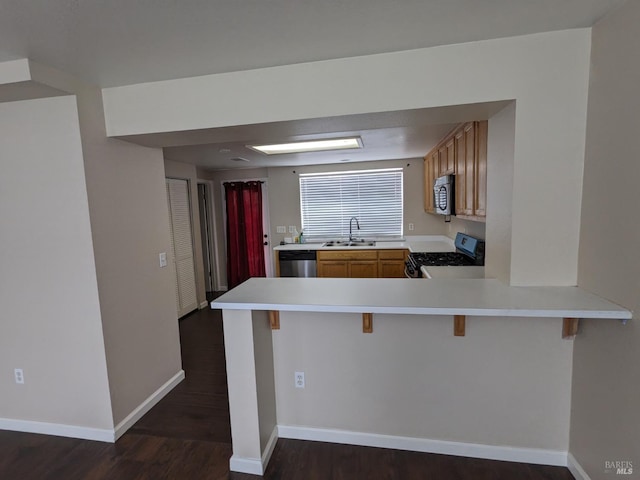 kitchen with light countertops, a peninsula, appliances with stainless steel finishes, and a sink