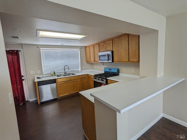 kitchen featuring dark wood-type flooring, a sink, stainless steel appliances, a peninsula, and light countertops