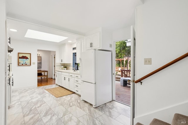 kitchen with light countertops, a skylight, freestanding refrigerator, white cabinets, and a sink