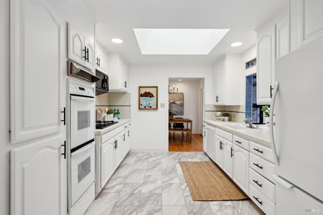 kitchen featuring white cabinetry, white appliances, a skylight, and a sink