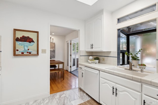 kitchen featuring a sink, tasteful backsplash, white cabinets, white dishwasher, and tile counters