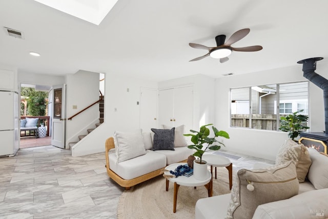 living area with visible vents, stairs, a skylight, a wood stove, and a ceiling fan