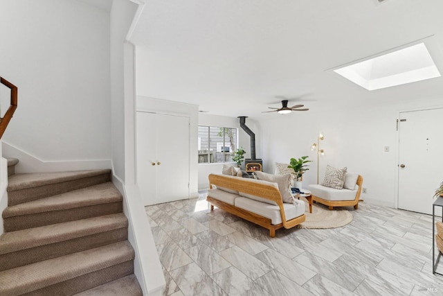 living area with stairway, a ceiling fan, baseboards, a skylight, and a wood stove