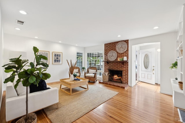 living room featuring light wood finished floors, visible vents, recessed lighting, and a brick fireplace