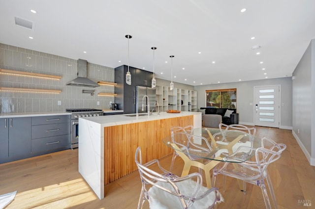 kitchen with a spacious island, stainless steel range, modern cabinets, wall chimney exhaust hood, and a sink