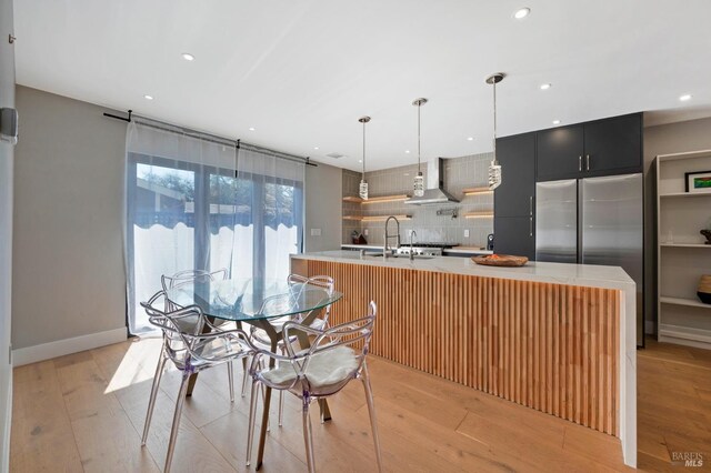 kitchen featuring light countertops, wall chimney exhaust hood, and light wood finished floors