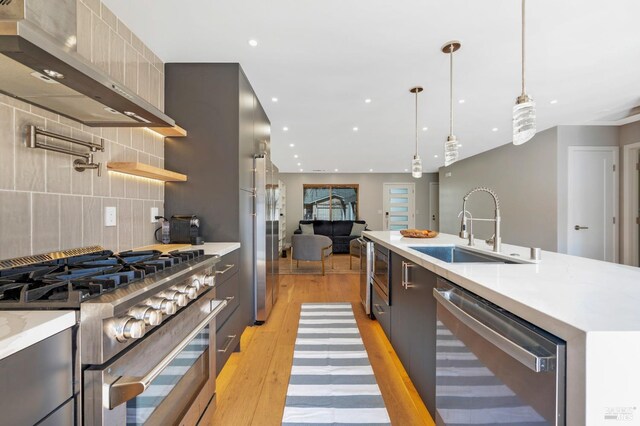 kitchen featuring light wood finished floors, appliances with stainless steel finishes, modern cabinets, wall chimney exhaust hood, and a sink