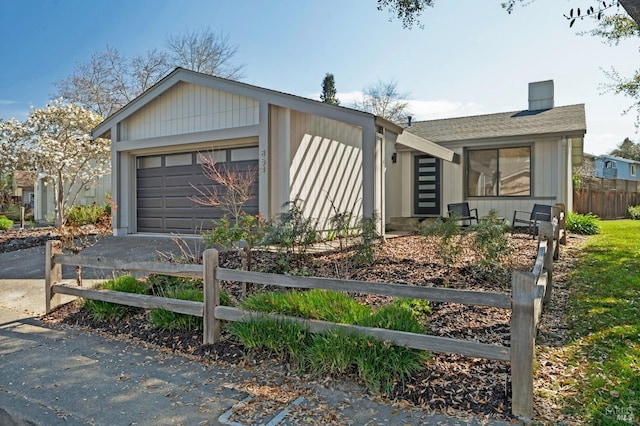 view of front of house featuring driveway, a chimney, an attached garage, and fence