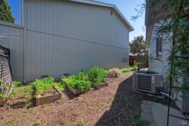 view of side of property featuring crawl space, central air condition unit, a garden, and fence