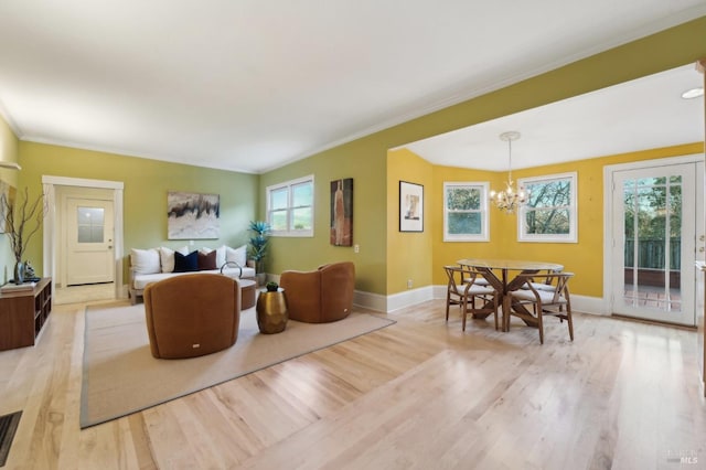 living room featuring light wood finished floors, baseboards, ornamental molding, and a notable chandelier