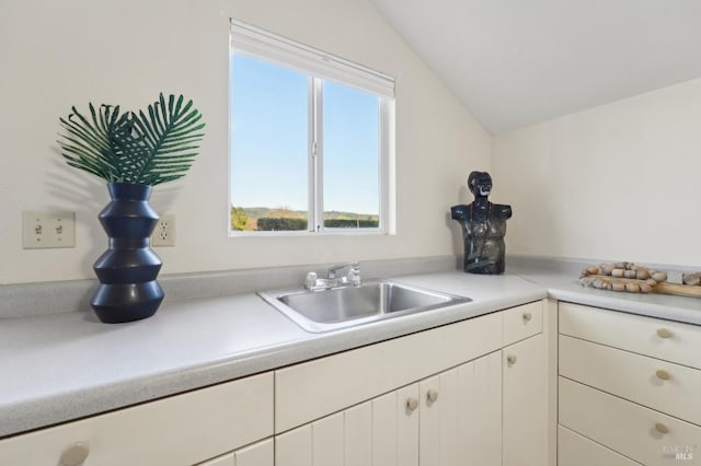 kitchen featuring light countertops, white cabinetry, lofted ceiling, and a sink