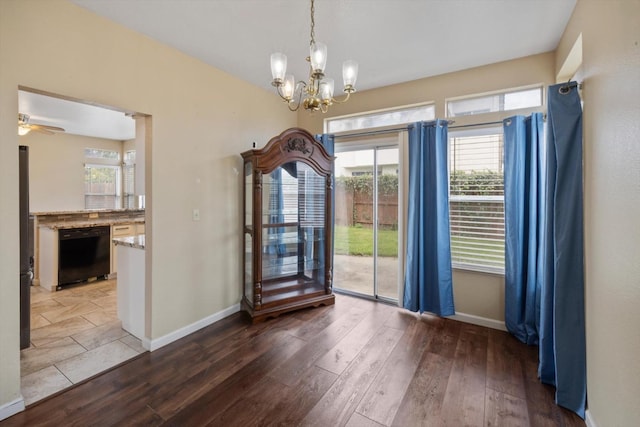 unfurnished dining area with ceiling fan with notable chandelier, baseboards, and wood finished floors