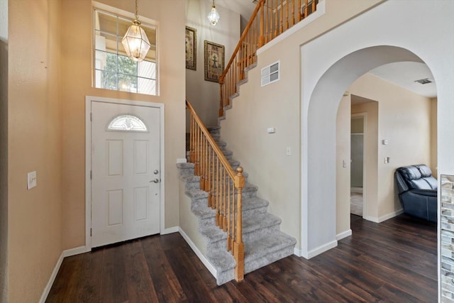 entryway featuring arched walkways, visible vents, a high ceiling, and wood finished floors