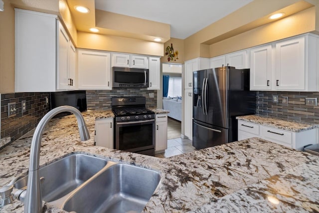 kitchen with a sink, light stone counters, appliances with stainless steel finishes, and white cabinets