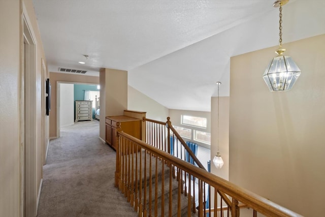 hallway with visible vents, carpet floors, lofted ceiling, an upstairs landing, and a chandelier