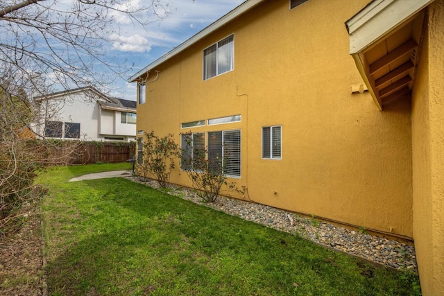 back of house featuring a lawn, fence, and stucco siding