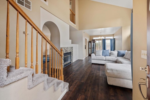 living room featuring visible vents, a tiled fireplace, stairway, an inviting chandelier, and dark wood-style floors