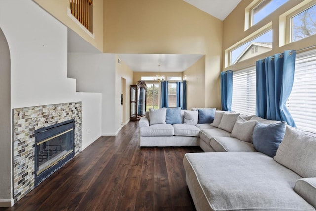 living room featuring high vaulted ceiling, a glass covered fireplace, wood finished floors, an inviting chandelier, and baseboards