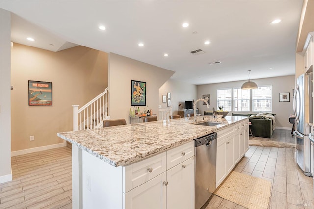 kitchen featuring visible vents, stainless steel appliances, a sink, an island with sink, and open floor plan