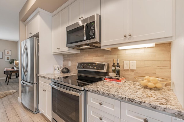 kitchen with backsplash, white cabinetry, light stone countertops, appliances with stainless steel finishes, and light wood-style floors