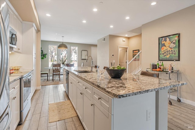 kitchen with white cabinets, a sink, an island with sink, and wood tiled floor