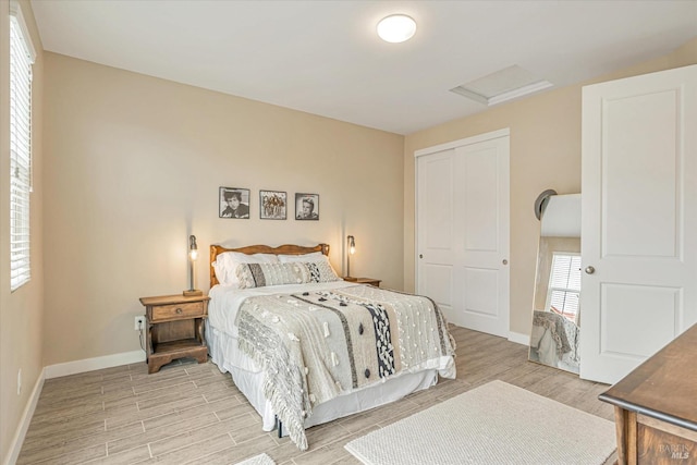 bedroom with a closet, baseboards, light wood-style floors, and attic access