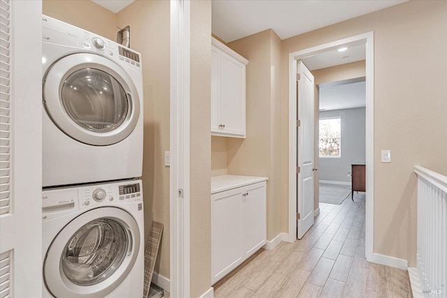 clothes washing area with baseboards, stacked washer and clothes dryer, laundry area, and wood finish floors