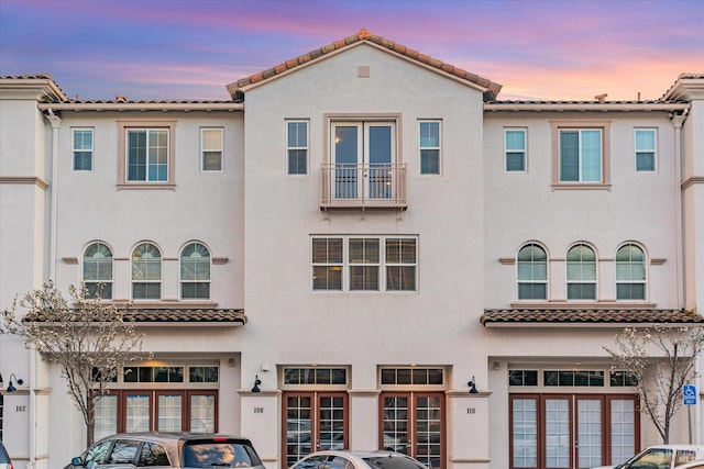 view of front of house featuring stucco siding, an attached garage, a tiled roof, and french doors