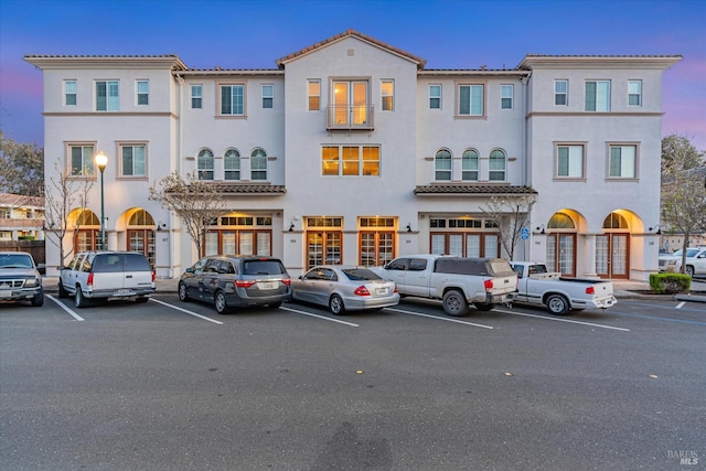view of front of house with stucco siding, uncovered parking, a tiled roof, and french doors