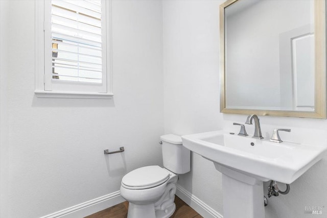 half bathroom featuring toilet, wood finished floors, baseboards, and a sink
