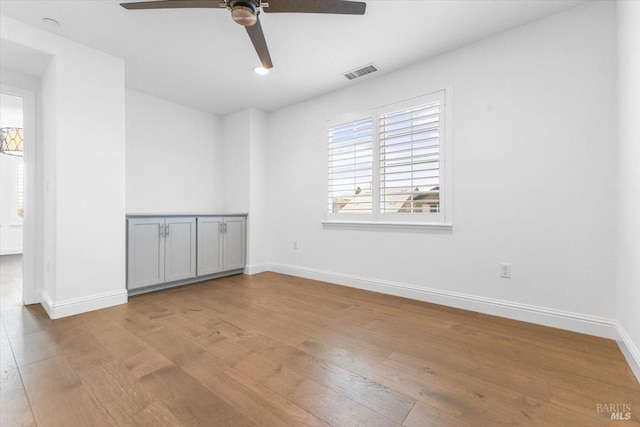 unfurnished room featuring a ceiling fan, wood finished floors, visible vents, and baseboards