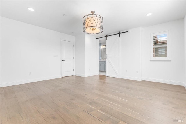 unfurnished room with recessed lighting, baseboards, light wood-type flooring, and a barn door