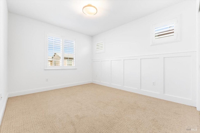spare room featuring light colored carpet, wainscoting, and a decorative wall