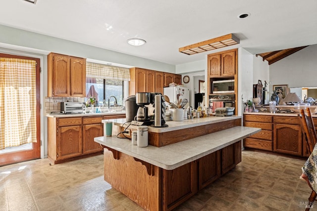 kitchen featuring freestanding refrigerator, a sink, light countertops, stainless steel microwave, and brown cabinets