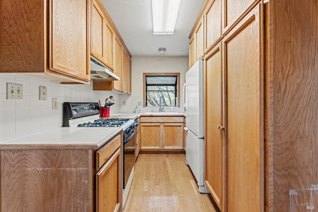 kitchen featuring under cabinet range hood, light wood-type flooring, freestanding refrigerator, gas stove, and a sink